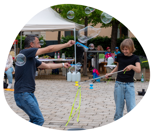 Ein Bild von zwei Menschen, die auf einem Straßenfest große Seifenblasen machen.