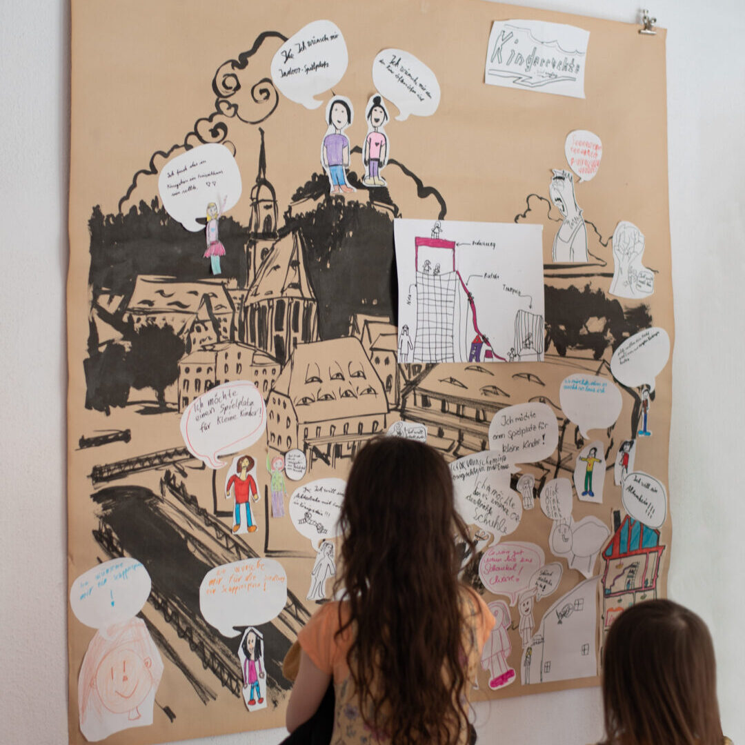 Zwei Kinder stehen vor einer Pinnwand mit bunten Kartekarten.