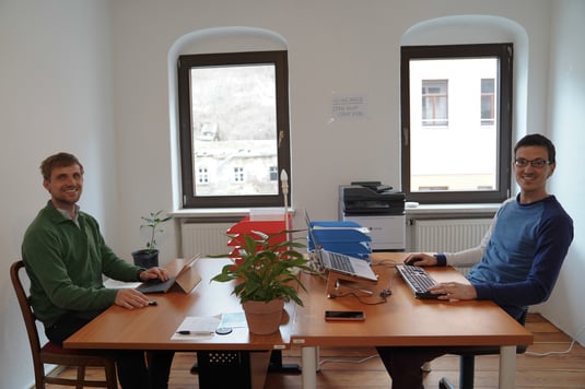 Zwie Männer sitzen in einem Büro mit zwei Schreibtischen