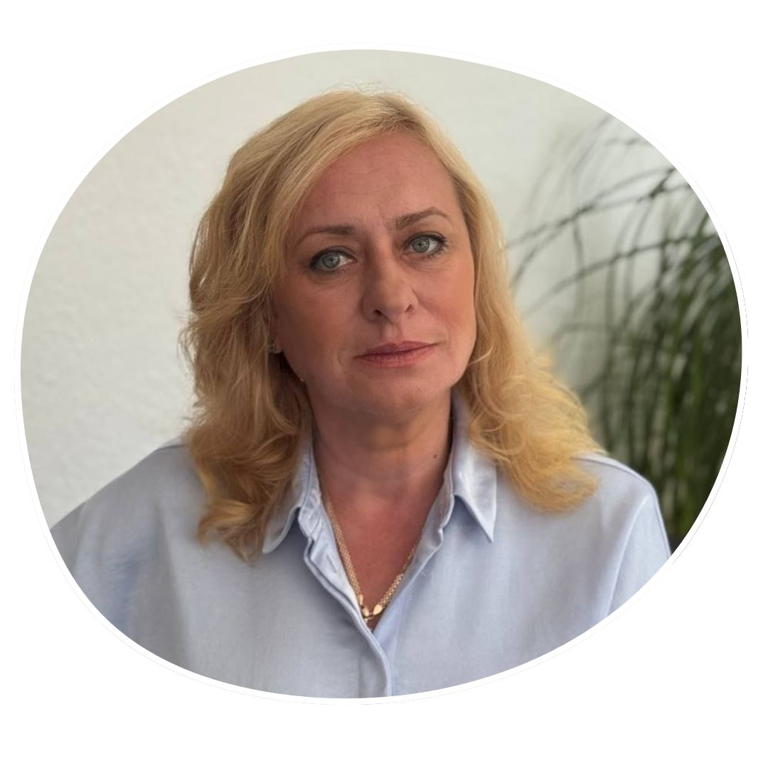 Inna Tyshkevych, hat schulterlange blonde Haare und grau-blaue Augen. Sie eine hellblaue Bluse an und trägt eine Goldkette um den Hals.