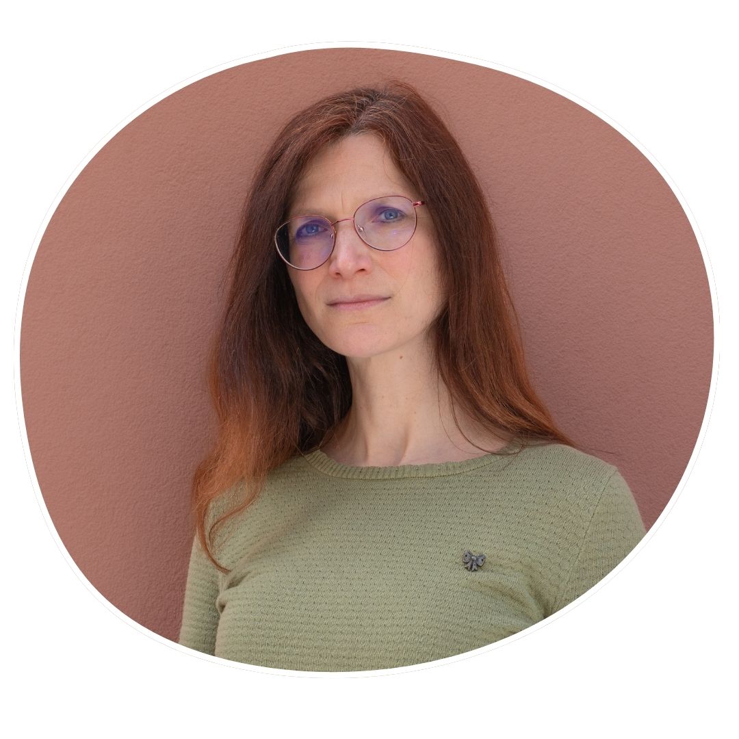 Yvonne, hat langes glattes rotbraunes Haar, sie hat helle Haut und trägt eine Brille.